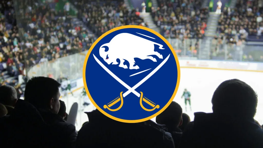 Buffalo Sabres logo centered over a blurred view of a crowded indoor hockey arena, with spectators silhouetted in the foreground and players on the ice in the background.