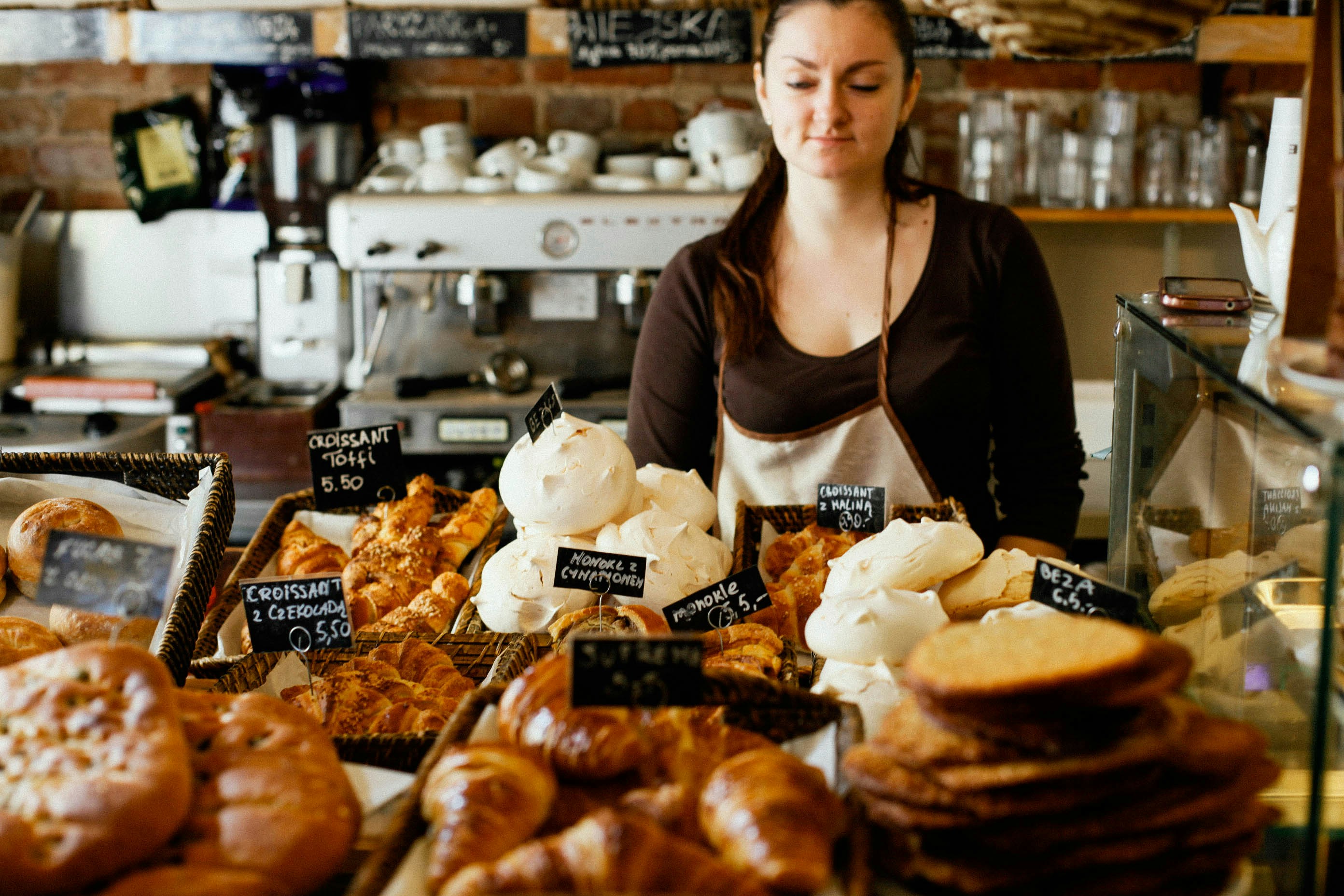 Bakery employee standing behind a display of fresh pastries, highlighting customer experience and operational excellence in franchise locations.
