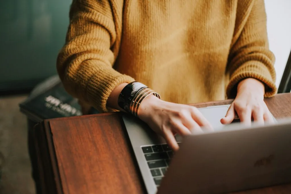 Woman in orange sweater typing on computer